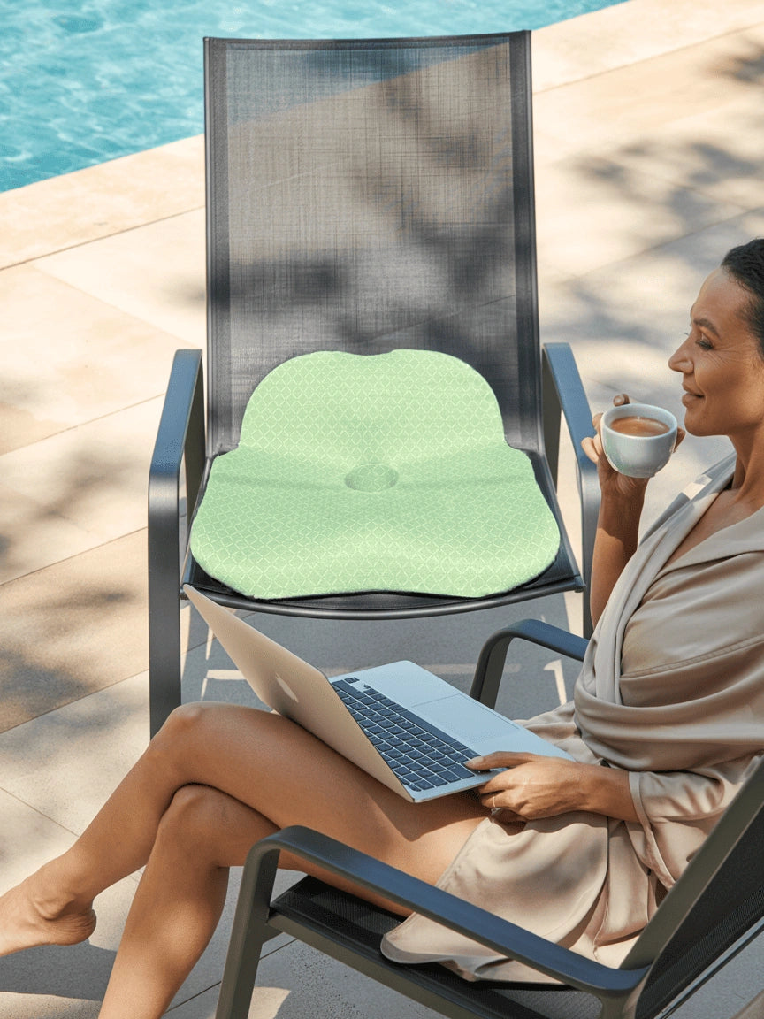 Woman using a laptop with a green posture cushion,Soothe, on a chair by a pool