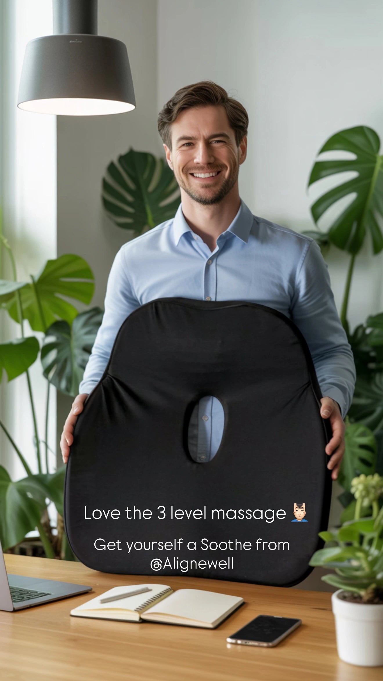 Man holding a black seat (posture cushion) cushion - Soothe- with plants and a desk in the background