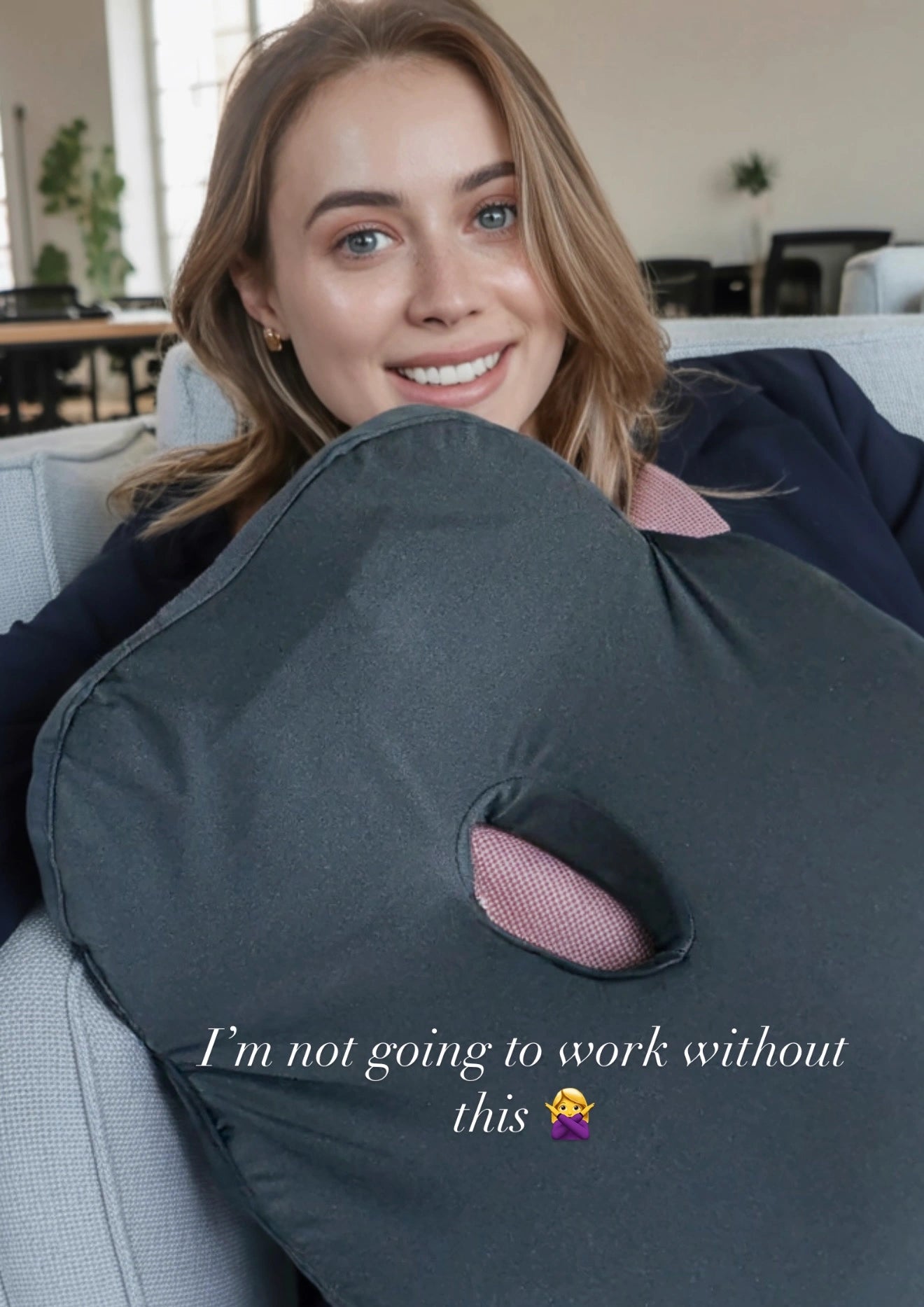 Woman holding a black seat cushion (posture cushion)-Soothe-  with a pink interior, smiling, in a home setting.